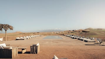Paisaje desértico con piscina, sillas de descanso y yurtas.