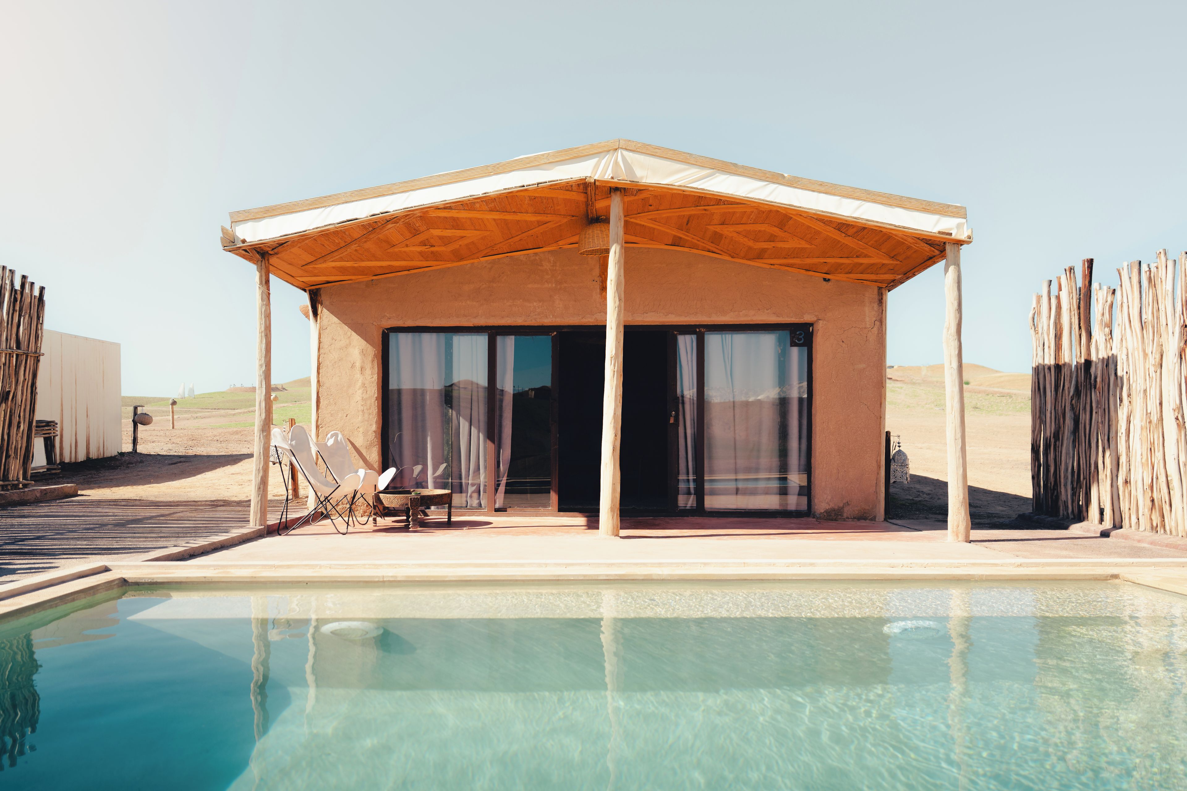 A poolside building with a covered patio, a pool, and a desert landscape in the background.