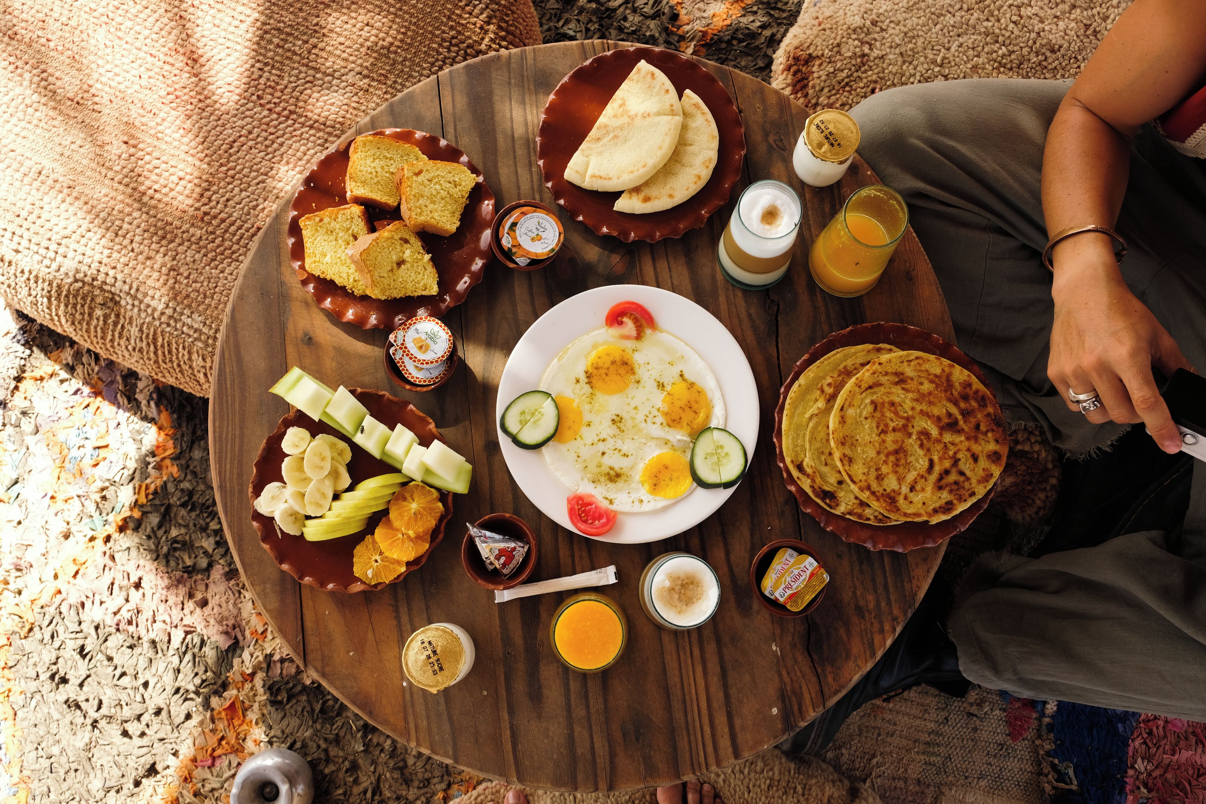 A round wooden table with various breakfast items including toast, eggs, and fruit.
