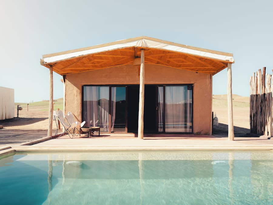 A poolside building with a covered patio, a pool, and a desert landscape in the background.
