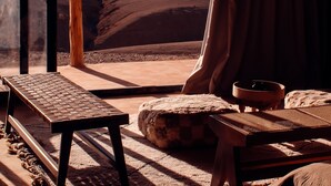 A room with a view of a desert landscape, a wooden bench, a small table, and a cushion. - Alkamar Camp Agafay (Agafay)