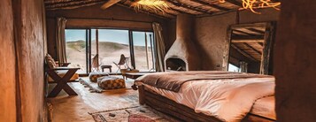 A cozy room with a large bed, a rustic fireplace, and a view of the desert outside.