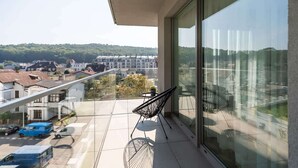 Un balcón con puerta de vidrio, una silla y vista a un pueblo con edificios y árboles.