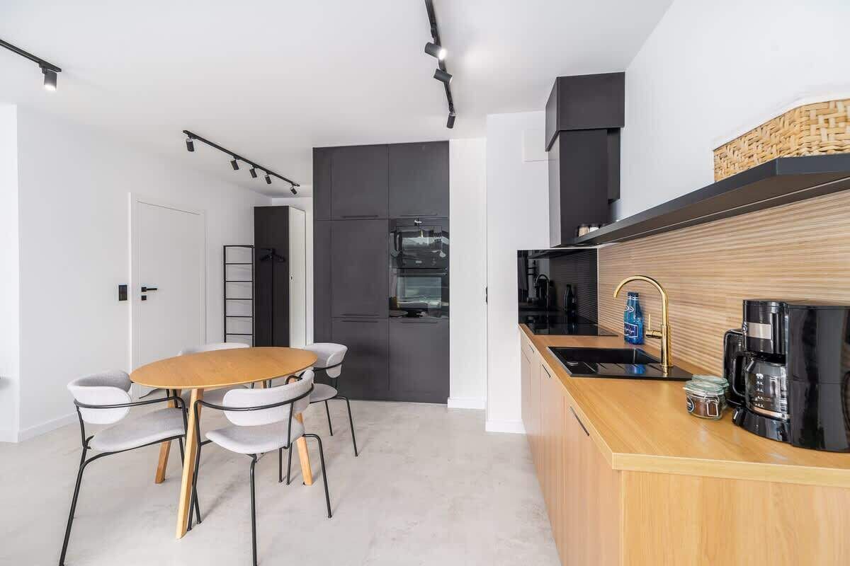 A modern kitchen with a wooden dining table and chairs, a built-in oven, and a coffee station.