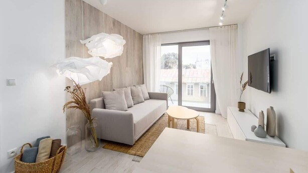 Un salon moderne avec un canapé gris, une table basse blanche et une grande fenêtre avec des rideaux.