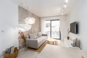 A modern living room with a grey sofa, a white coffee table, and a large window with curtains.