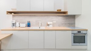 Une cuisine moderne avec des armoires blanches, un plan de travail en bois, un four encastré et une machine à café.