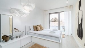Une chambre moderne avec un grand lit, une table de chevet, un miroir et une vue sur l’extérieur grâce à une grande fenêtre.