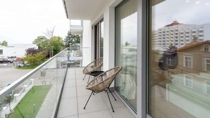 Un balcon avec deux fauteuils en osier, de grandes fenêtres et une vue sur la mer et les bâtiments.