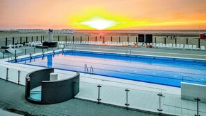 Une piscine avec vue sur le coucher de soleil, des chaises longues et une fontaine circulaire.