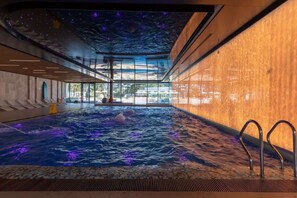 Une piscine intérieure avec un plafond étoilé et une vue sur l’extérieur.