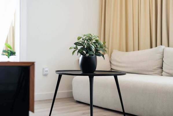 Una sala de estar con un sofá color crema, una mesa redonda negra con una planta en maceta y un mueble para televisión.