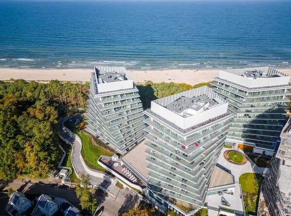 Un hôtel moderne à plusieurs étages, doté d’une terrasse sur le toit et offrant une vue sur la plage et l’océan.