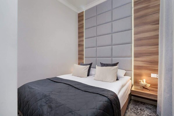 A modern bedroom with a large bed, a padded headboard, and a nightstand with a decorative bird sculpture. - Stylish Apartment | Air Conditioning | Close to the Old Town (Kraków)