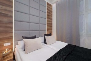 A modern bedroom with a tufted headboard, a bed with white and black bedding, and a wooden accent wall. - Stylish Apartment | Air Conditioning | Close to the Old Town (Kraków)