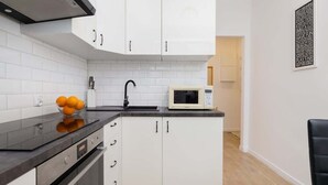 A modern kitchen with white cabinets, a black countertop, a microwave, and a bowl of oranges. - Comfortable Apartment with Bedroom | Work Space (Gdańsk)
