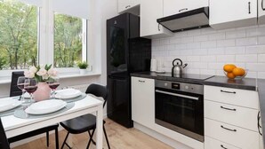 A modern kitchen with white cabinets, a black refrigerator, and a dining area with a table set for two. - Comfortable Apartment with Bedroom | Work Space (Gdańsk)