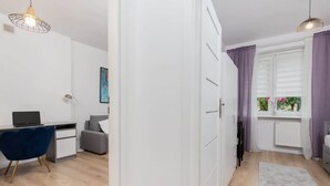 A modern, well-lit room with a desk, chair, and a view of the outdoors through a window with purple curtains. - Comfortable Apartment with Bedroom | Work Space (Gdańsk)