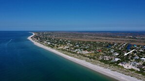 Vista aérea de un pueblo costero con una playa extensa, zona residencial densa y cielos azules despejados.
