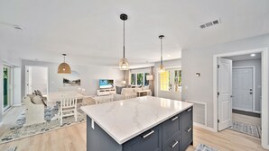 Una cocina amplia con una isla grande, lámparas colgantes modernas y un comedor con vistas al exterior.