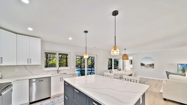 Una cocina moderna con armarios blancos, una isla grande y un área de comedor con vista a la piscina.
