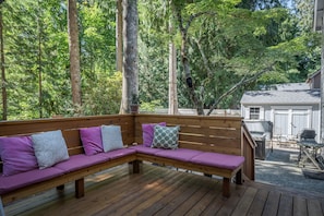 A wooden deck with a built-in bench, surrounded by tall trees. - Beautiful home in a quiet neighborhood, Hot tub, big backyard! (Welches)