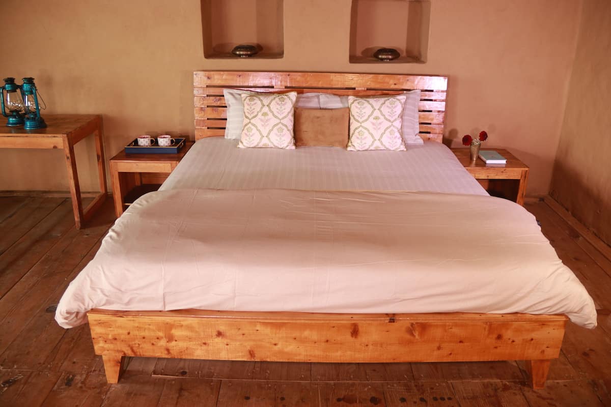 A wooden bed with a white mattress and patterned pillows, flanked by nightstands with a tray and a vase of flowers.