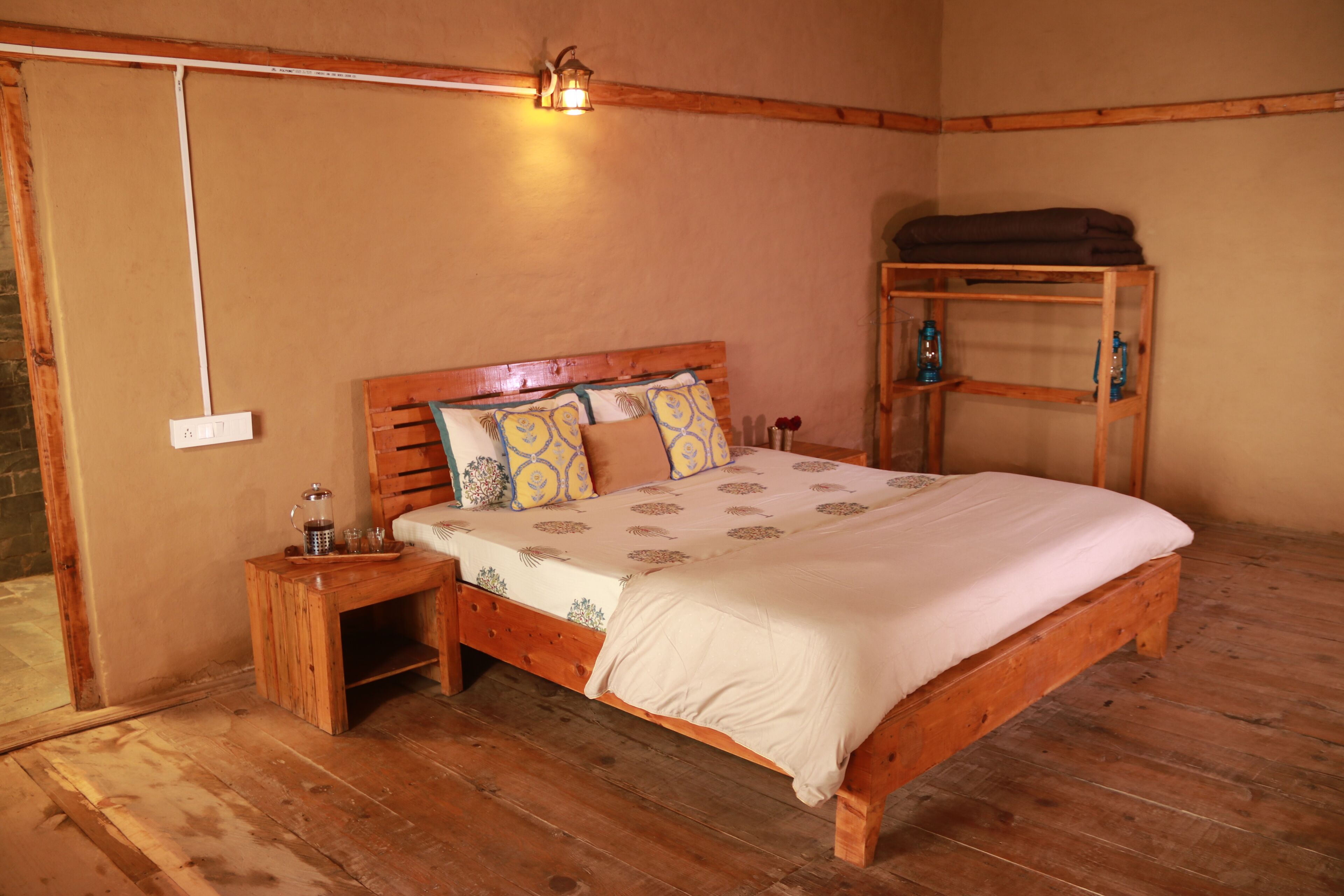 Una cama de madera con cabecera, una mesita de noche con lámpara y una estantería con botellas.