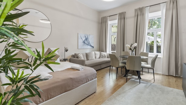 A modern, well-lit room with a bed, a sofa, a dining table with chairs, and a large window with curtains. - Stylish Apartments near AKH (Vienna)