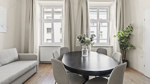 A room with a round table, six chairs, a sofa, and two windows with curtains. - Stylish Apartments near AKH (Vienna)
