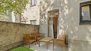 A patio with wooden furniture, a stone wall, and a building with a window and door. - Stylish Apartments near AKH (Vienna)