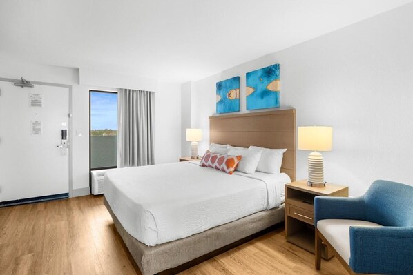 A hotel room with a large bed, two bedside lamps, a blue armchair, and two abstract paintings on the wall.