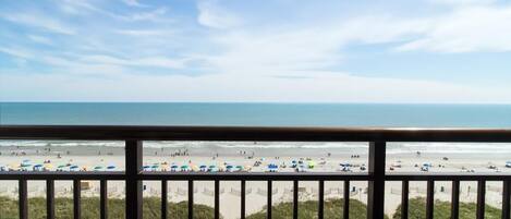 Une vue sur la plage depuis un balcon doté d’une balustrade, avec une plage de sable et l’océan en toile de fond.