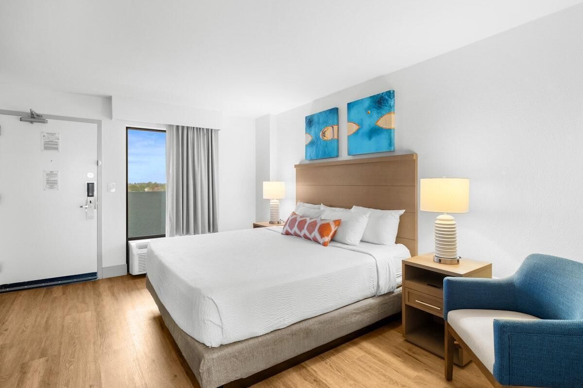 Een hotelkamer met een groot bed, twee bedlampen, een blauwe fauteuil en twee abstracte schilderijen aan de muur.
