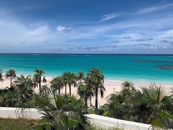 A beach with clear turquoise water, palm trees, and a white building in the foreground.