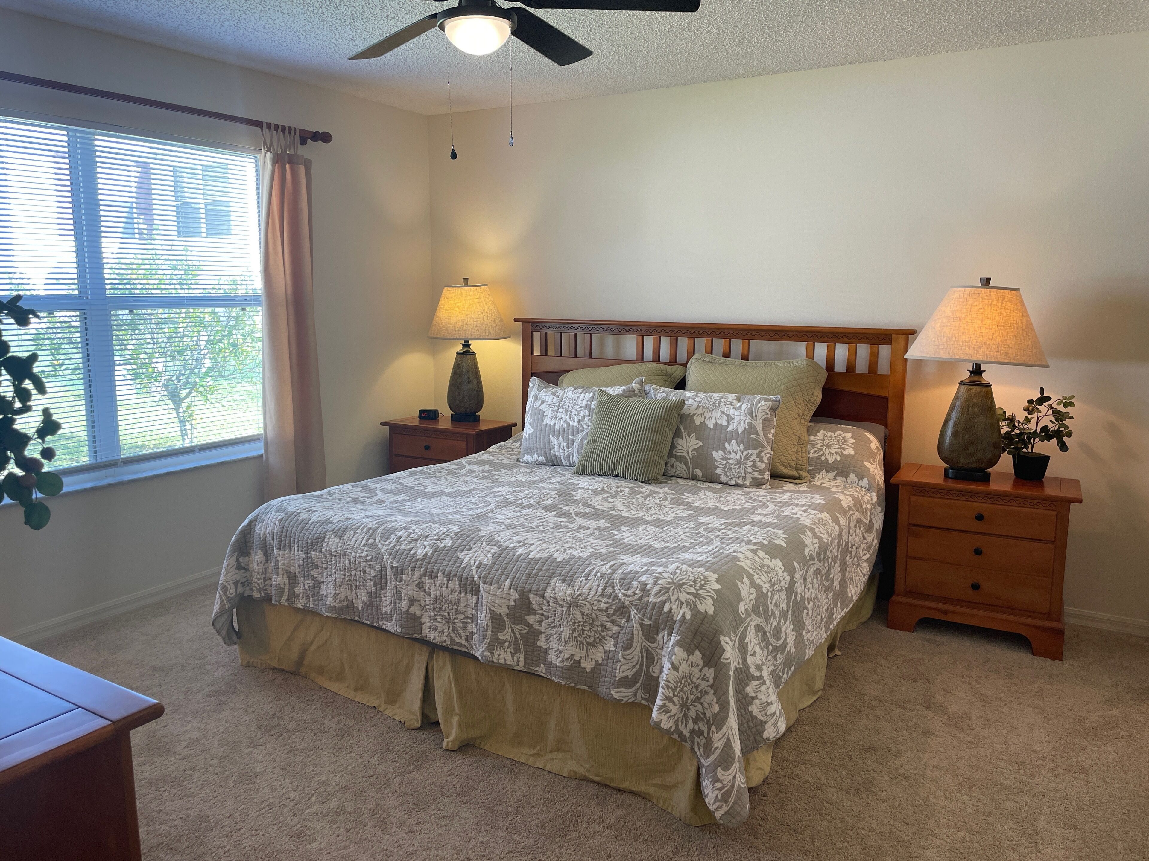 A bedroom with a bed, two nightstands, a ceiling fan, and a window with blinds.
