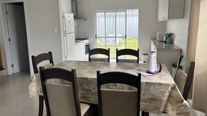 A dining area with a table and chairs, a kitchen in the background, and a view of the outdoors. - Casa Relax 3 (Paysandú)