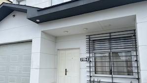 A modern building with a white facade, a garage door, a white door, and a window with a metal grill. - Casa Relax 3 (Paysandú)