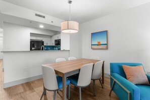 A modern kitchen with white cabinets, a wooden dining table, and a blue sofa. - Newly Renovated 17th Flr Oceanfront 2 Bedroom (Myrtle Beach)