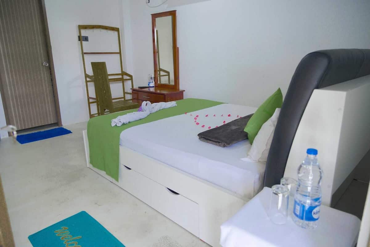 A hotel room with a bed, a nightstand, a mirror, a chair, and a desk with a water bottle and glasses.