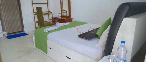 Habitación de hotel con cama, mesita de noche, espejo, silla y escritorio con una botella de agua y vasos.