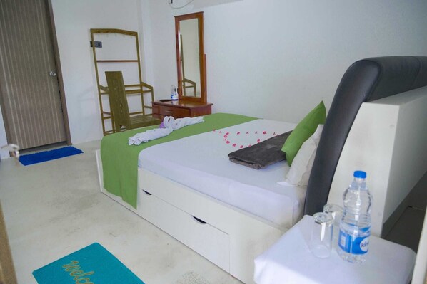 A hotel room with a bed, a nightstand, a mirror, a chair, and a desk with a water bottle and glasses.