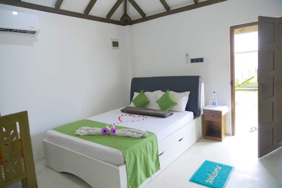 A neatly arranged bedroom with a bed, a bedside table, a chair, and a door leading outside.