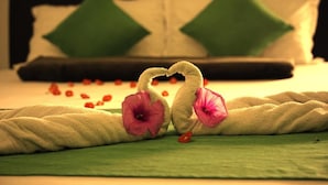 Una cama bien hecha con una colcha verde y blanca, dos almohadas verdes y una decoración con forma de corazón hecha de tela.