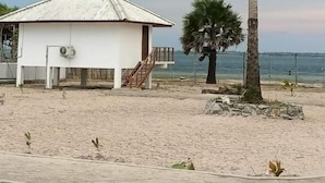 Un pequeño edificio blanco con techo de metal, una escalera que lleva a un balcón y una palmera cercana.
