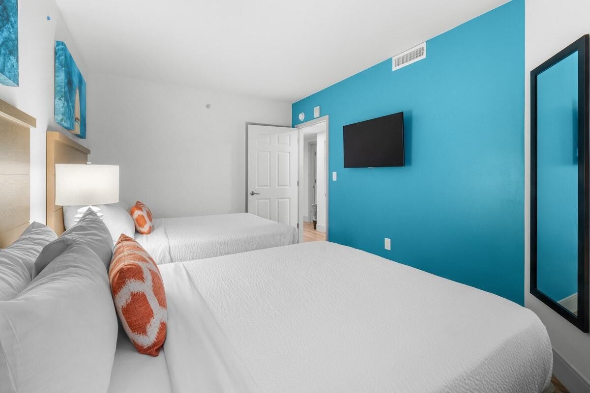Une chambre d’hôtel avec deux lits, un téléviseur fixé au mur et une porte donnant sur une autre pièce.