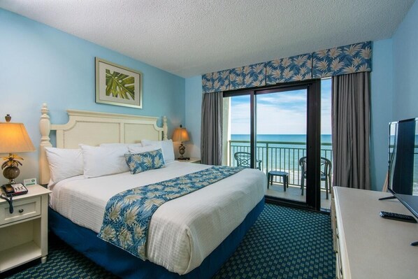 Une chambre d’hôtel avec un grand lit, un bureau, une télévision et un balcon donnant sur la mer.