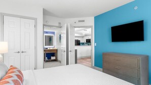 A bedroom with a bed, a dresser, a TV, and a bathroom visible through an open door. - Newly Renovated 7th Floor 2 Bedroom Condo (Myrtle Beach)