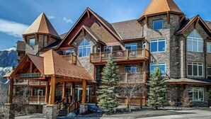A multi-story lodge with a stone facade, multiple balconies, and a prominent entrance with stairs. - Hope Peak Hydeaway at Stoneridge (Canmore)