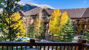 A wooden deck with a table and chairs, overlooking a pool and a mountain backdrop. - Hope Peak Hydeaway at Stoneridge (Canmore)